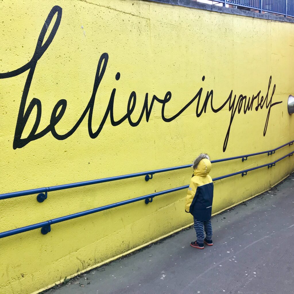 A little boy contemplating a sign that says 'believe in yourself' to show self-efficacy. 